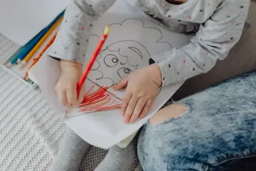 Mały rysunek dziecka z kredkami. Dziecko koloruje czerwoną kredką.