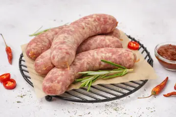 Surowa biała kiełbasa na ruszcie z rozmarynem, papryczkami chili i sosem. Dowiedz się, ile gotować białą kiełbasę, by była idealna.