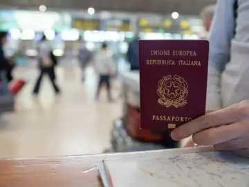 Włoski paszport w dłoni, na tle lotniska. Czy do Wiednia potrzebny jest paszport? Tak, jeśli nie jesteś obywatelem UE.