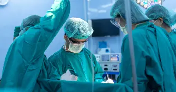 Zespół chirurgów w zielonych fartuchach i czepkach pracuje przy stole operacyjnym. Zmiana lekarza specjalisty w trakcie leczenia jest kluczowa dla powodzenia operacji.