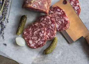 Kawałki aromatycznego salami napoli, ogórki konserwowe, cebulka i gałązka lawendy na papierze.