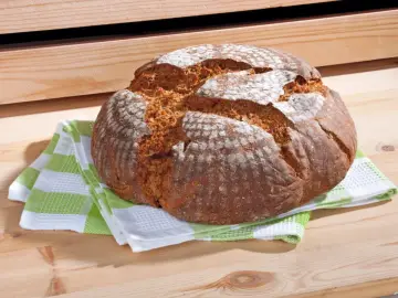 Chleb na drewnianym stole, na zielono-białej ściereczce.