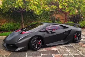 Matowy czarny Lamborghini Sesto Elemento z czerwonymi akcentami i wnętrzem, zaparkowany na brukowanej ścieżce wśród zieleni.
