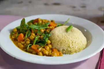 Un plato de cuscus con verduras, garbanzos y zanahoria en una salsa dorada, decorado con hojas verdes.