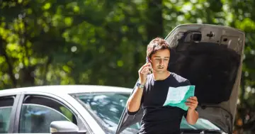 Mężczyzna z dokumentem w ręku dzwoni po assistance na wyjazd, gdy jego samochód uległ awarii.