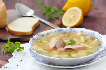Zupa śledziowa Ani gotuje się w tle, z kawałkami ryby, ziemniaków i marchewki. Obok leżą cytryny i kromka chleba.