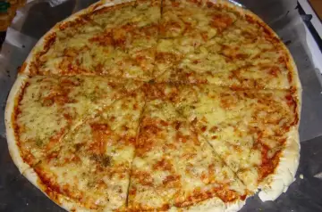 Pyszna pizza margerita z ciągnącym się serem i aromatycznymi ziołami, pokrojona na 8 kawałków.