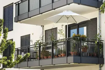 Nowoczesny balkon po remoncie, z białym parasolem i doniczkami pełnymi zieleni.