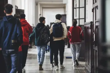 Uczniowie w szkolnym korytarzu, z plecakami, idący w stronę, kiedy składa się papiery do liceum.