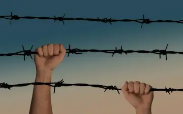 Dwie dłonie zaciskają się na drutach kolczastych, symbolizując walkę o wolność i nadzieję na amnestia.