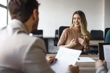 Uśmiechnięta kobieta podczas rozmowy kwalifikacyjnej, która może zakończyć się podpisaniem umowy na czas nieokreślony.