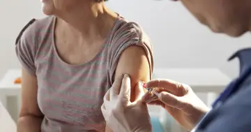 Osoba w rękawiczkach podaje zastrzyk w ramię starszej kobiety. Choć szczepionka Pfizer jest bezpieczna, niektórzy doświadczają skutków ubocznych.