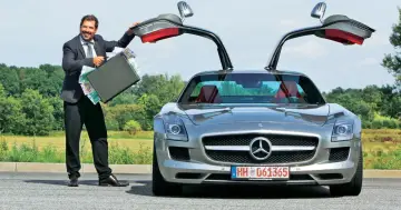 Szczęśliwy mężczyzna w garniturze otwiera drzwi swojego SLS AMG, prezentując walizkę pełną pieniędzy.