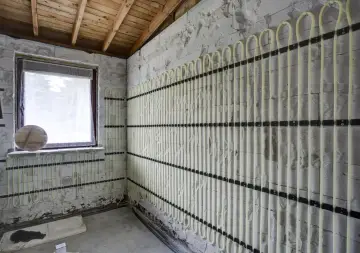 Instalacja ogrzewania ściennego wodnego w trakcie budowy. Jasne rurki ułożone pionowo i poziomo na ścianie z bloczków.