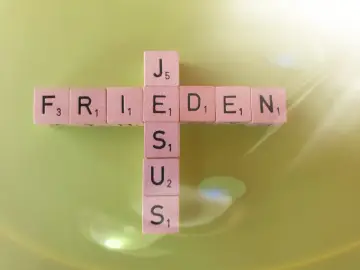 Buchstabensteine bilden ein Kreuz mit den Wörtern "FRIEDEN" und "JESUS". Ein Zitat aus Johannes 14.