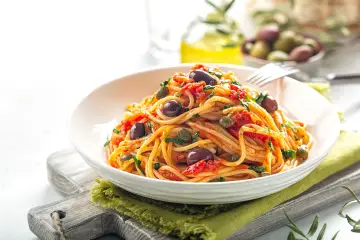 Un piatto invitante di spaghetti alla puttanesca, con olive nere, capperi e pomodoro, pronto per essere gustato.