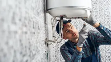 Instalator w rękawiczkach dokręca śrubę w bojlerze.