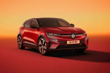 Nowy Renault Megane 5 w kolorze czerwonym, z czarnym dachem, prezentuje się dynamicznie na tle pomarańczowo-czerwonego gradientu.