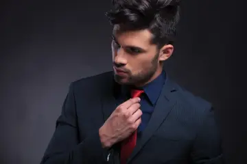 Ein Mann im schwarzen Anzug mit blauem Hemd und roter Krawatte, der seine Krawatte richtet.