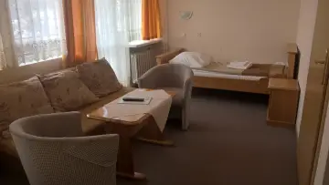 Pokój w sanatorium uzdrowiskowym „Leśnik”. Wygodna kanapa, stolik z pilotem, łóżko i krzesła.