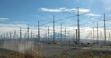 Ogromne pole anten HAARP pod błękitnym niebem, z górami w tle.
