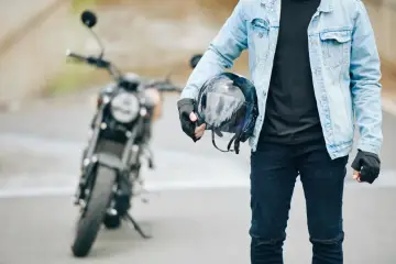Gotowy na jazdę nowym motocyklem. W ręku trzyma kask, ubrany w jeansową kurtkę i rękawiczki.