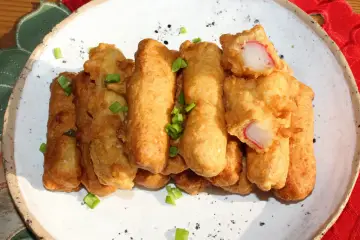 Chrupiące paluszki surimi w cieście, posypane szczypiorkiem, prezentują się apetycznie na białym talerzu.
