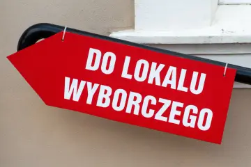 Czerwona strzałka z białym napisem "DO LOKALU WYBORCZEGO". Wskazuje drogę do miejsca, gdzie można oddać głos, przypominając o tym, ile trwa kadencja wójta.