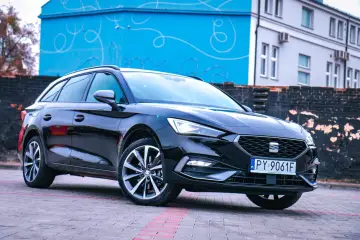 Czarny Seat Leon Sportstourer z polskimi tablicami rejestracyjnymi stoi na brukowanym placu przed budynkiem z niebieską, ozdobną ścianą.