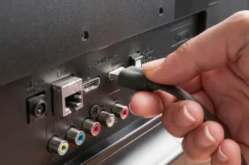 Dłoń podłącza kabel do portu HDMI ARC w telewizorze, zapewniając dźwięk przestrzenny.
