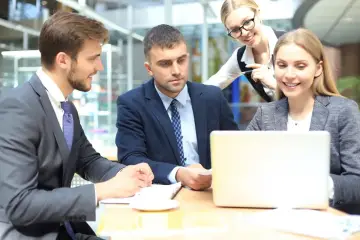 Zespół przy biurku analizuje dane. Młody pracownik młodociany uczy się od starszych kolegów.