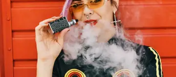 Joven con vaper exhala humo. ¿Cuántas calorías tiene un vaper? La respuesta es cero, ya que no contiene azúcares ni grasas.