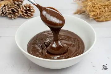 Cuchara con ganache de chocolate cayendo en un cuenco blanco. El chocolate es brillante y sedoso, perfecto para postres.
