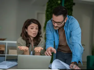 Para dyskutuje o 800 plus dla uczących się po 18 roku życia, analizując dokumenty przy laptopie.