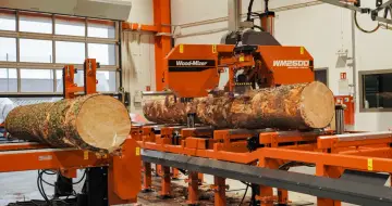 Pomarańczowa maszyna do obróbki drewna Wood-Mizer WM2500 przetwarza pień drzewa na deski.