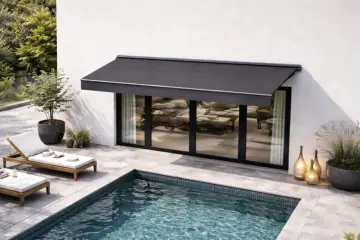 Un store banne gris protège une terrasse moderne avec piscine. L'entretien de ce store est essentiel pour profiter de cet espace de détente.