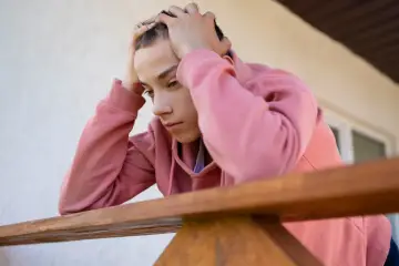 Nastolatek z rękami wplątanymi we włosy, zamyślony. Objawy silnego stresu u nastolatków mogą być widoczne w jego postawie.