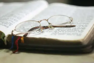 Okulary spoczywają na otwartej księdze, symbolizując chwilę refleksji i modlitwy. Wierzę w Boga, a ta księga jest moim przewodnikiem.