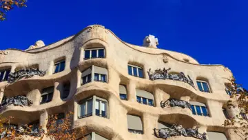 Falista fasada Casa Mila w Barcelonie, z kamienia i kutego żelaza, pod błękitnym niebem.