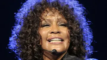 Whitney Houston z zamkniętymi oczami, w pełni emocji, pokazuje niesamowitą **skalę głosu**.