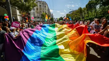 Tęczowa flaga niesiona przez tłum podczas marszu, symbolizująca dumę i wsparcie dla społeczności LGB.
