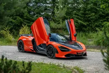 Pomarańczowy McLaren 720S z otwartymi drzwiami, zaparkowany na kamienistej drodze. Jego cena jest wysoka, ale wrażenia bezcenne.