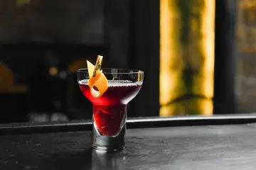 Elegancki drink czarny rusek, ozdobiony skórką pomarańczy, kusi głębokim kolorem na barze.