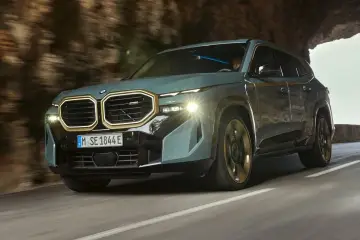 Nowoczesne BMW XM w kolorze szaro-zielonym przemierza krętą drogę, wyłaniając się z tunelu.