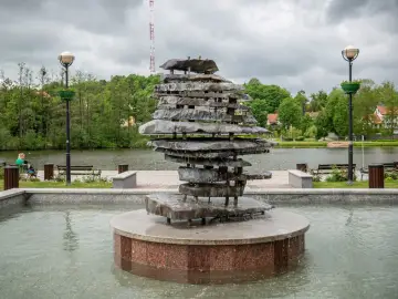 Kamienna rzeźba-fontanna nad jeziorem, jedna z atrakcji Czosu. W tle drzewa i budynki.