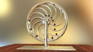 Glänzendes Rad mit schwarzen Kugeln, das an ein Perpetuum mobile erinnert, steht auf einem Holztisch.