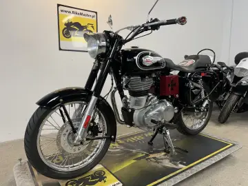 Klasyczny czarny Royal Enfield 500 z chromowanymi elementami i czerwonym krzyżem na bocznej skrzynce.