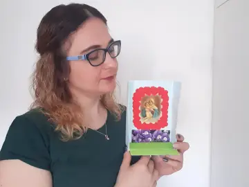 Kobieta trzymająca w rękach ozdobną kapliczkę z wizerunkiem Matki Boskiej i kwiatów.