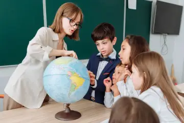 Nauczycielka pokazuje uczniom globus, wyjaśniając im świat. Dzieci z zaciekawieniem słuchają lekcji geografii.