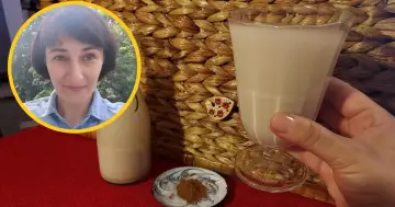 Kobieta z uśmiechem prezentuje szklankę z wodą owsianą, obok butelka i cynamon.